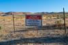 A landscape of dry mountainous grassland with clear blue sky. A sign in on a barb wire fence in the foreground says: Access Restricted/ Active Mine Site/Thacker Pass Project/ For access please call Lithium Nevada Corp