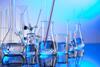 Various types of laboratory glassware, a thermometer and stirrers sitting on a surface with a blue background